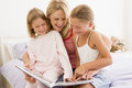 Woman and two young girls in bedroom reading book Stock Image