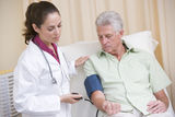 Doctor checking man's blood pressure in exam room Stock Images