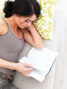 Young woman lying on sofa at home reading book Stock Photos