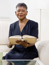 African woman reading book on sofa in livingroom Stock Photos