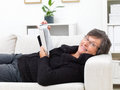 Happy mature woman lying on a sofa reading a book Royalty Free Stock Photo