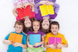 Happy kids laying on the floor holding books Stock Photos