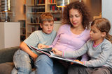 Children with mother sit on sofa and read book Royalty Free Stock Image