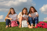 Three girls sit on grass and read something Stock Images