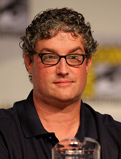 A man with glasses and a red shirt sits in front of a microphone.
