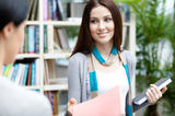 Undergraduate offers a book to her friend Stock Photo